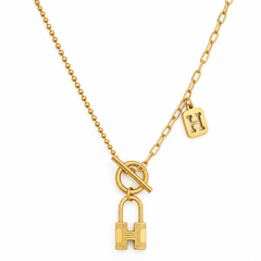 Gold necklace featuring a beaded chain with a toggle clasp, a link chain segment with a small square 'H' charm, and a larger padlock-shaped 'H' pendant, shown on a white background.
