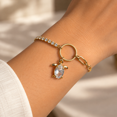 A gold bracelet with a small turtle charm and clear rhinestone details, shown worn on a person's wrist.