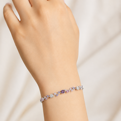 A delicate silver-toned bracelet with clear and lavender-purple crystals, worn on a person's wrist against a soft, light beige background.