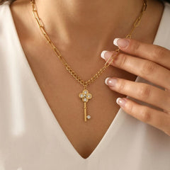 A close-up of a woman wearing a gold key pendant necklace with clear rhinestone accents, styled with a white V-neck top.