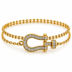 A gold-tone double-strand bracelet featuring a central horseshoe-shaped clasp paved with clear crystals, set against a clean white background.