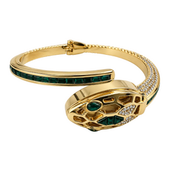 A gold snake-head cuff bracelet featuring green emerald-cut stones and pavé diamonds, displayed on a clean white background.