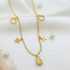 A gold-toned double-strand necklace with a small padlock pendant, floral clover charms, and square ring charms, styled on a cream satin fabric with scattered white pearls.