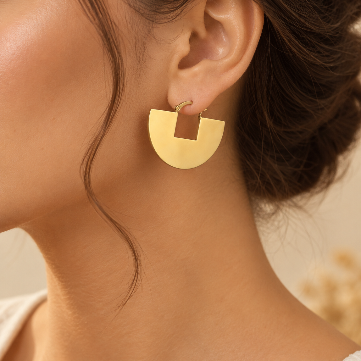 A close-up of a model wearing a gold geometric drop earring with a square cutout, shown against her ear and neck.