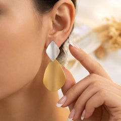 A close-up of a model wearing a modern geometric dangle earring with a textured silver diamond-shaped top and a brushed gold teardrop-shaped drop.