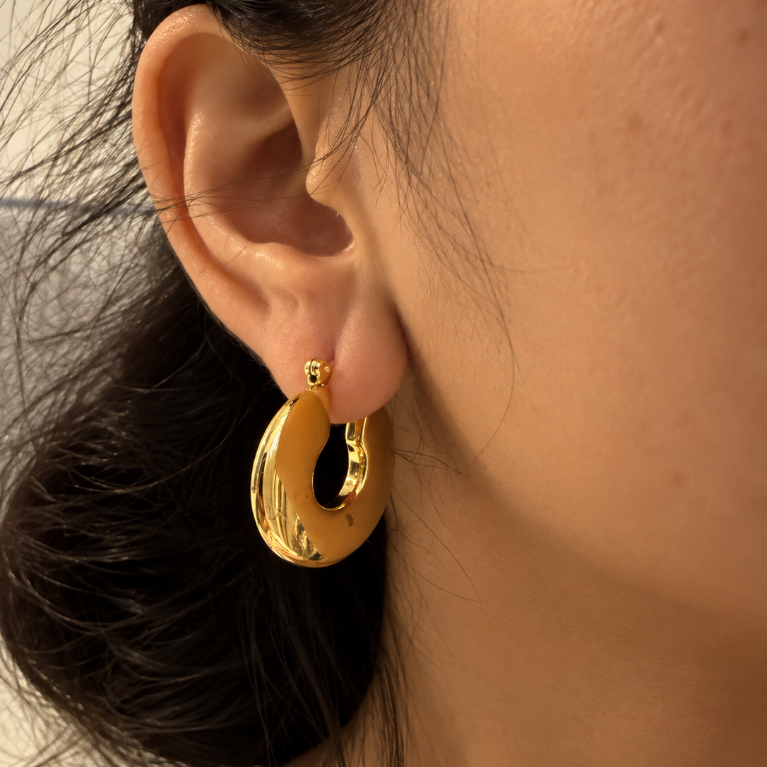 A close-up of a person's ear wearing a chunky, polished gold hoop earring.