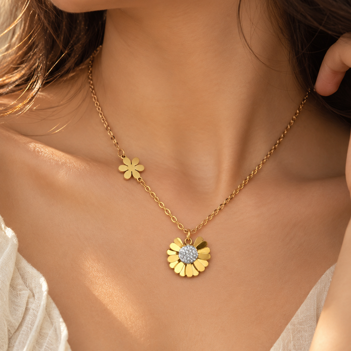 A close-up lifestyle shot of a model wearing a delicate gold chain necklace with two small flower charms and a larger flower pendant featuring a sparkling clear center.