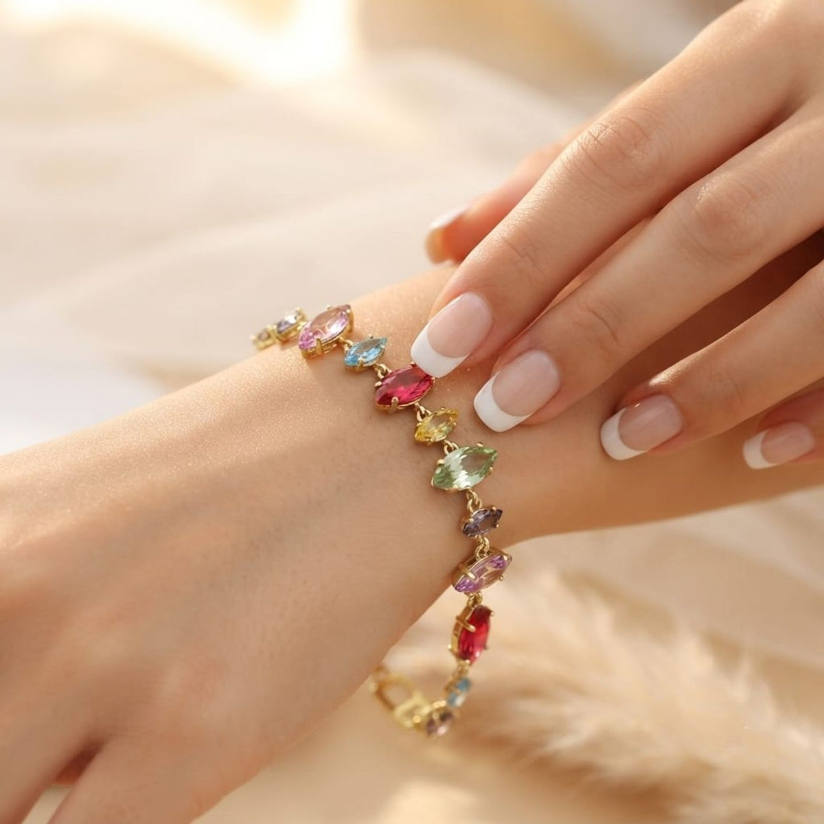 A gold-toned bracelet with multiple colorful gemstones, shown worn on a woman's wrist with her hand resting above it. The bracelet features marquise-cut stones in pink, blue, yellow, green, and purple on a gold chain.
