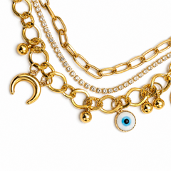 Gold-tone layered chain bracelet featuring a paperclip chain, a rhinestone-encrusted chain, evil eye charms, and crescent moon charms, displayed on a clean white background.