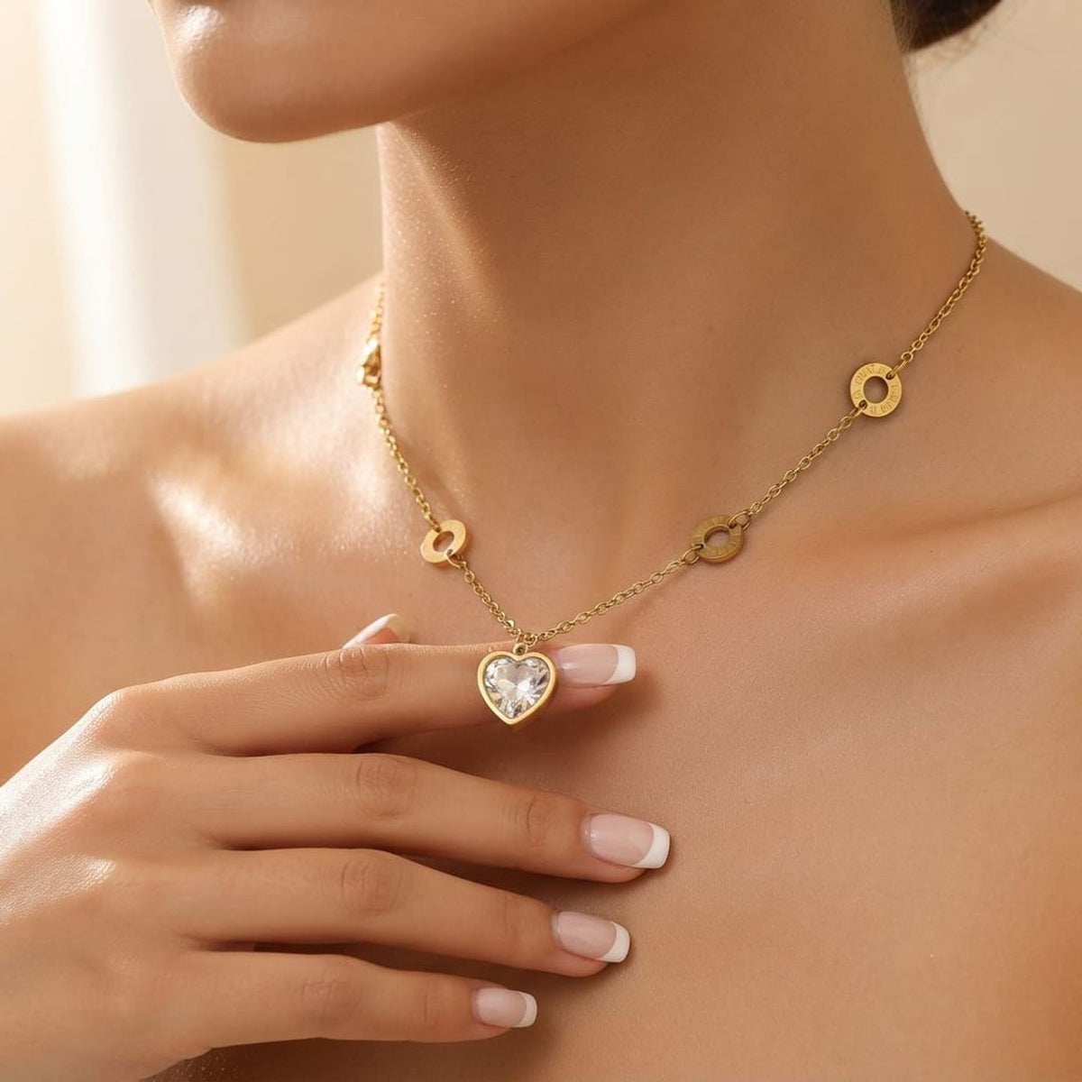A close-up of a model wearing a delicate gold chain necklace with a heart-shaped clear crystal pendant and small gold circle charms.