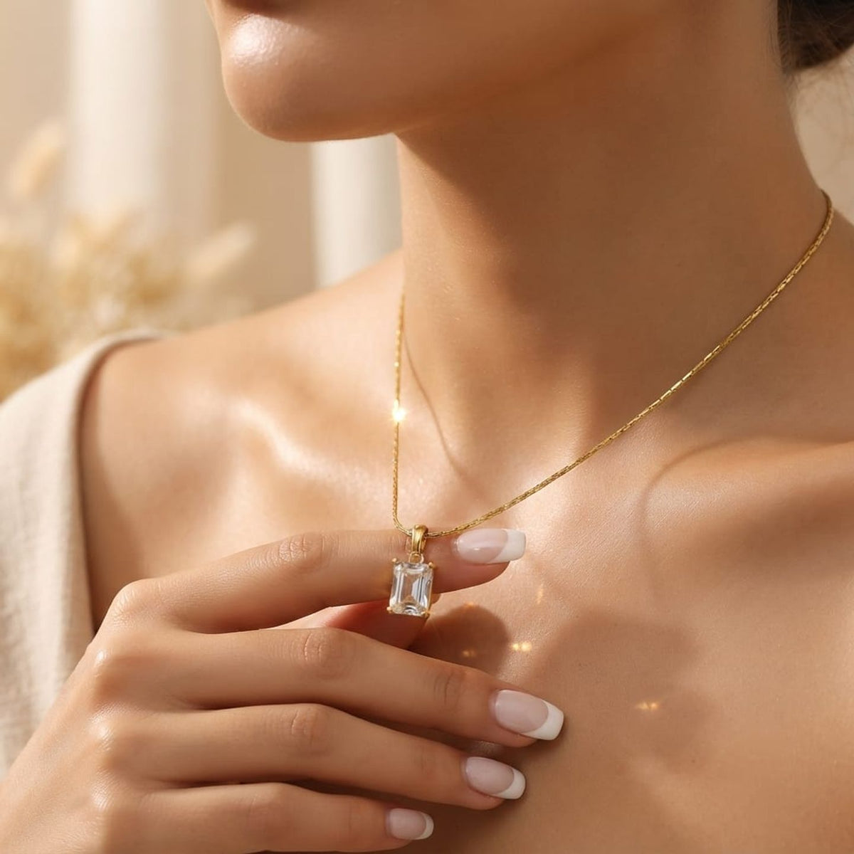 A close-up lifestyle shot of a woman wearing a delicate gold chain necklace with a rectangular clear gemstone pendant, resting her hand near the necklace.