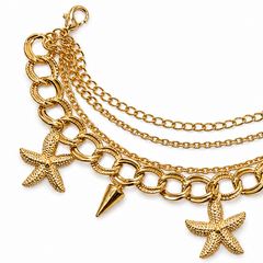 A gold-toned multi-layered chain necklace featuring starfish and spiked cone charms, displayed on a clean white background.