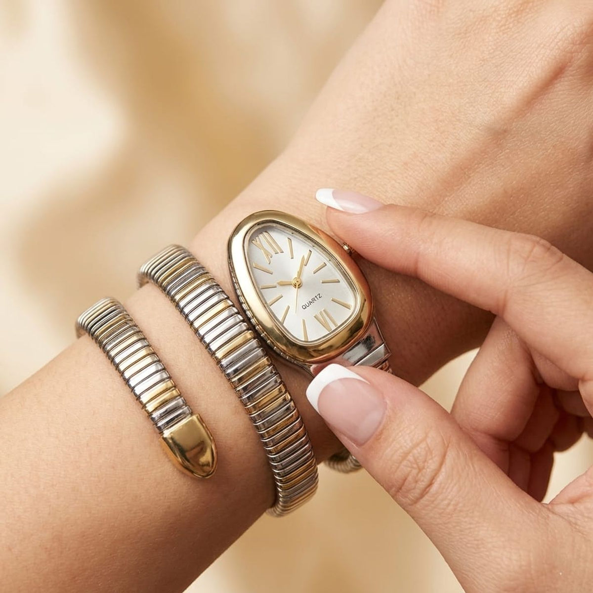 A close-up lifestyle shot of a woman's wrist wearing a gold and silver-tone watch with a white dial, alongside a matching two-tone bangle bracelet.
