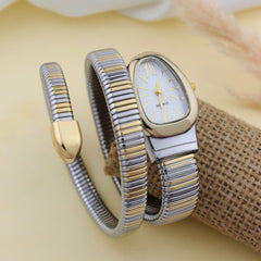 A two-tone silver and gold watch with a matching two-tone metal wrap bracelet, displayed on a beige surface with a burlap roll and soft fabric background.