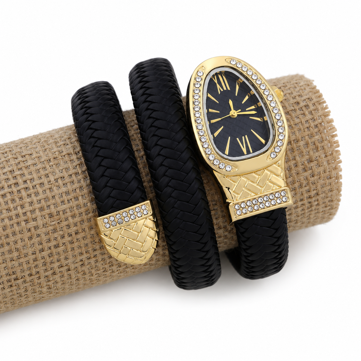 A gold and black wrap-style watch with a woven leather band, displayed on a burlap-wrapped cylinder against a white background.