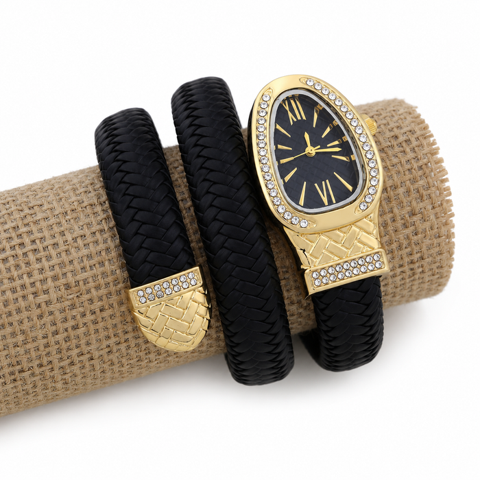 A gold and black wrap-style watch with a woven leather band, displayed on a burlap-wrapped cylinder against a white background.