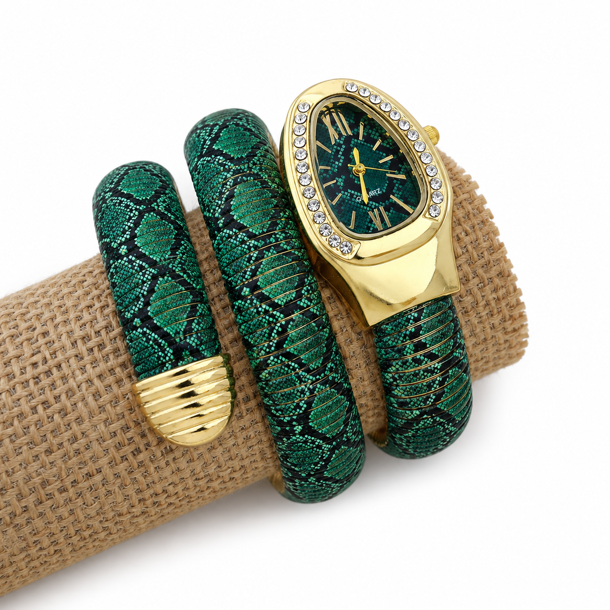 A gold-tone watch with a green textured strap and a matching green bangle bracelet, both featuring a snakeskin pattern, displayed on a burlap-wrapped ring stand against a white background.