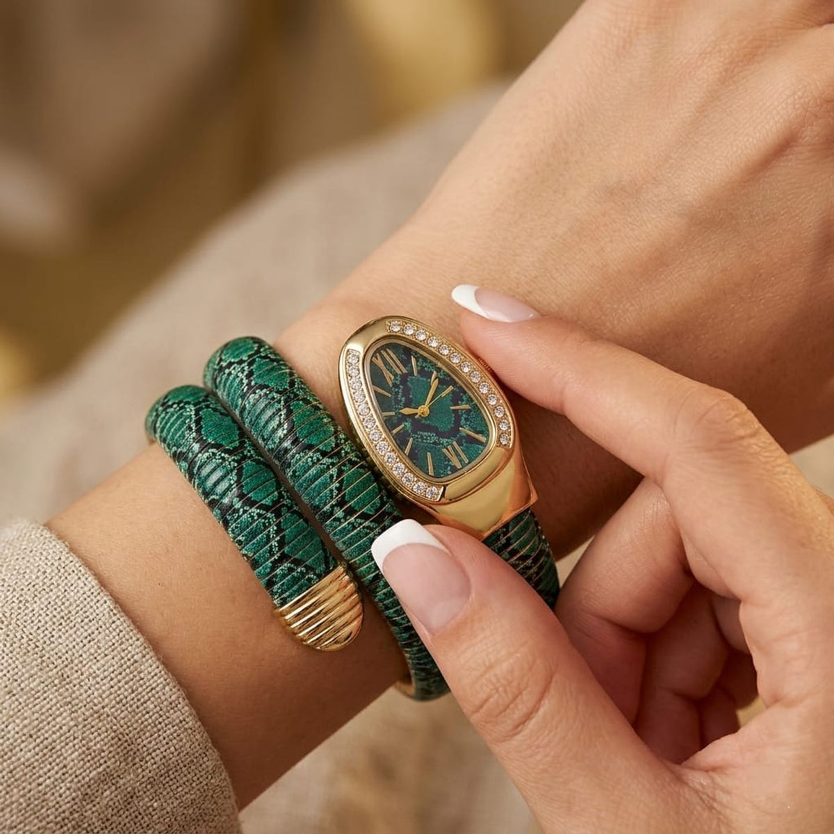 A close-up lifestyle shot of a woman's wrist wearing a green snake-print wrap bracelet and a gold-tone watch with a green dial and crystal accents.