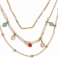 A gold multi-strand necklace featuring delicate chains, elongated bar links, small gold beads, and heart-shaped charms in light blue, pink, red, and clear crystal, displayed on a clean white background.