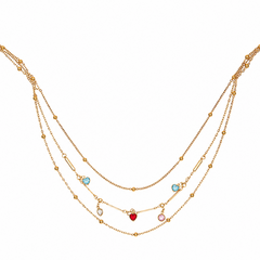 A multi-layered gold necklace featuring delicate chains, small bead accents, and three dangling charms: a red heart, a light blue oval, and a light pink oval, displayed on a clean white background.