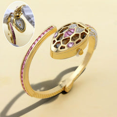 Gold snake-head bangle watch with pink and crystal accents, shown on a beige background with a circular inset close-up of the watch face.