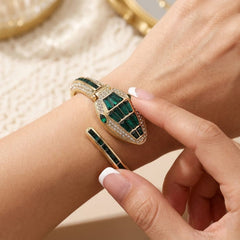 A close-up lifestyle shot of a gold-plated bangle bracelet with green malachite inlay and pavé-set clear crystals, shown worn on a wrist with a matching slim bangle.