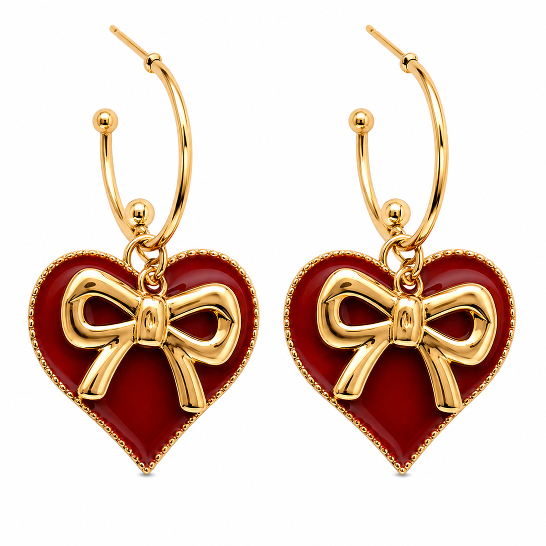 A pair of gold hoop earrings with heart-shaped dangles featuring a deep red enamel background and a raised gold bow motif, shown on a plain white background.