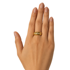 A gold ring with a channel-set row of small clear stones, worn on a hand with neutral pink manicured nails against a warm beige background.