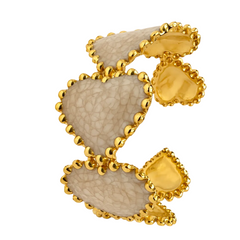 A sculptural cuff ring featuring textured beige stone inlays set in a polished yellow gold bezel with a beaded chain-link border, shown on a clean white background.