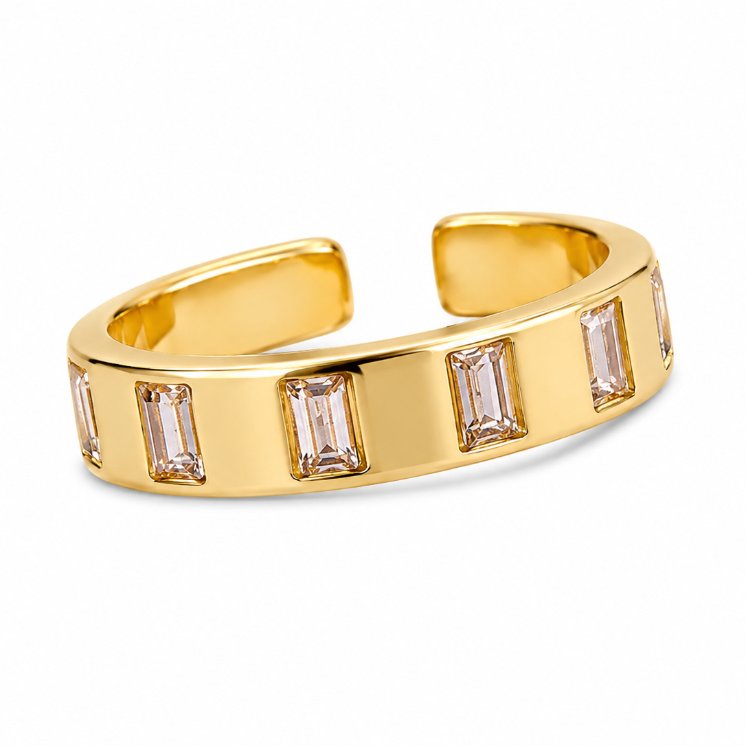 A gold-toned open cuff ring featuring a row of rectangular baguette-cut clear crystals, shown on a clean white background.