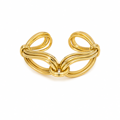 A polished gold-tone metal cuff bracelet with a sculptural, interlocking loop design, photographed on a seamless white background.