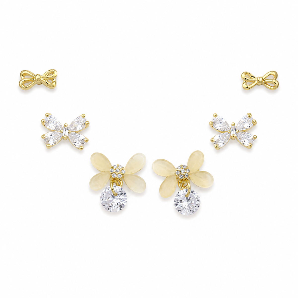 A set of five gold-tone stud earrings arranged on a white background, including two bow-shaped earrings, two butterfly-shaped earrings with clear rhinestones, and two flower-shaped earrings with pale yellow petals and clear rhinestones.