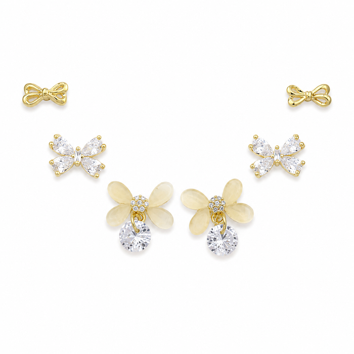 A set of five gold-tone stud earrings arranged on a white background, including two bow-shaped earrings, two butterfly-shaped earrings with clear rhinestones, and two flower-shaped earrings with pale yellow petals and clear rhinestones.