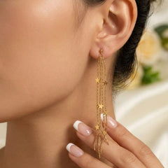 A close-up of a model wearing a long gold dangle earring with multiple star-shaped charms, with her hand gently touching the lower charm.