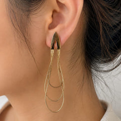 A close-up of a person's ear wearing a single gold-toned statement earring with a tapered top and layered teardrop loops below.