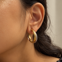 A close-up of a person's ear wearing a thick, twisted two-tone hoop earring in polished gold and silver.
