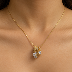 A close-up of a model's neck and chest wearing a delicate gold chain necklace with a pendant featuring clear gemstones.