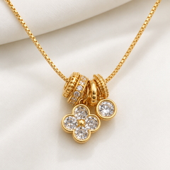 Gold chain necklace with a multi-component charm pendant featuring a flower motif and clear rhinestones, displayed on a soft white fabric background.